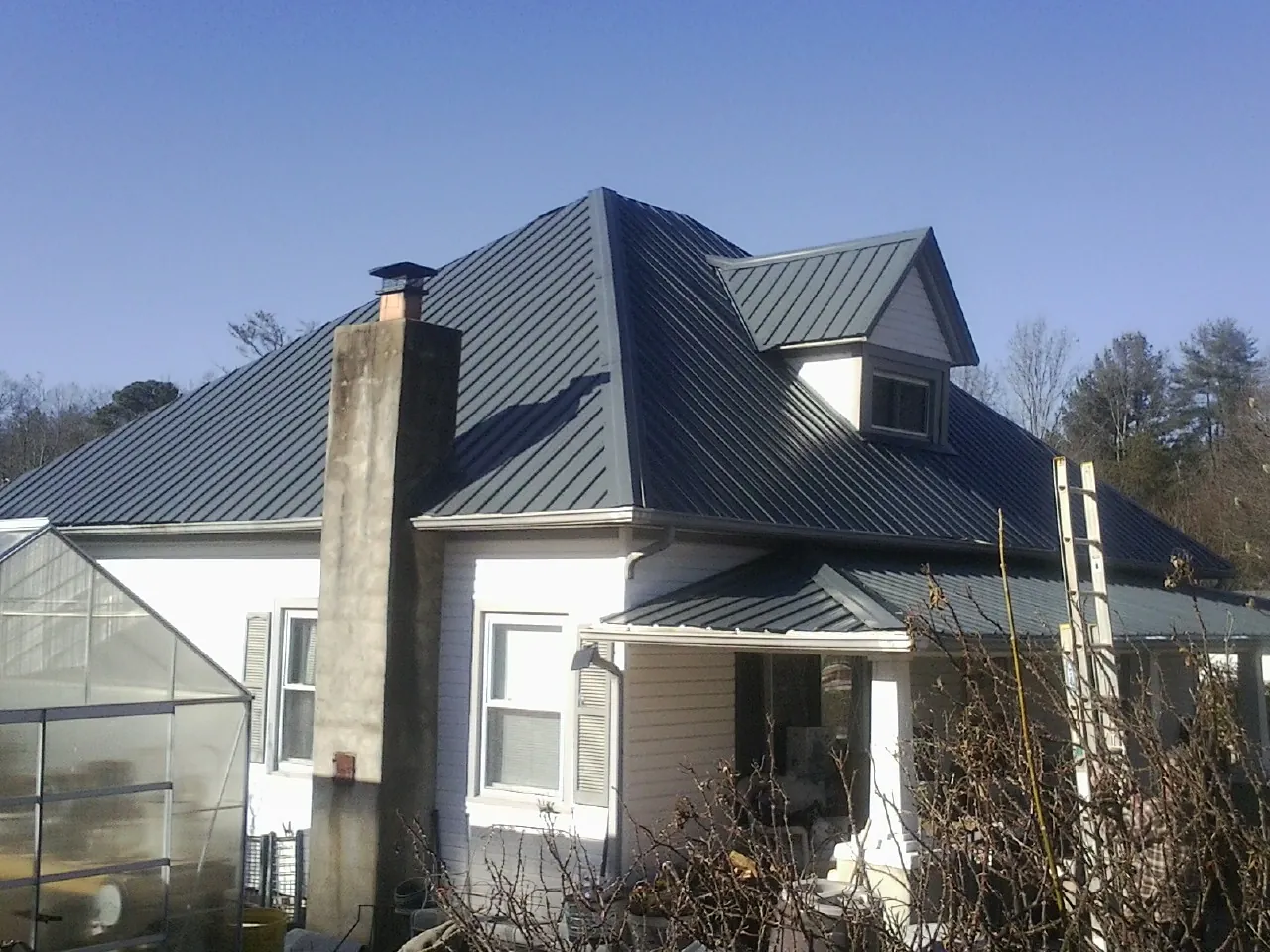 Dark blue standing seam metal roof on a white farmhouse with dormer — Slate & Tile Roof Repair by Roofing Brothers in Teton