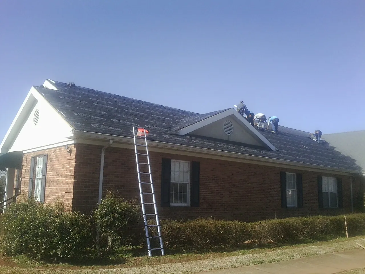 Crew tearing shingles off a brick ranch roof with a ladder set — Metal Roof Repair work by our crew in Teton