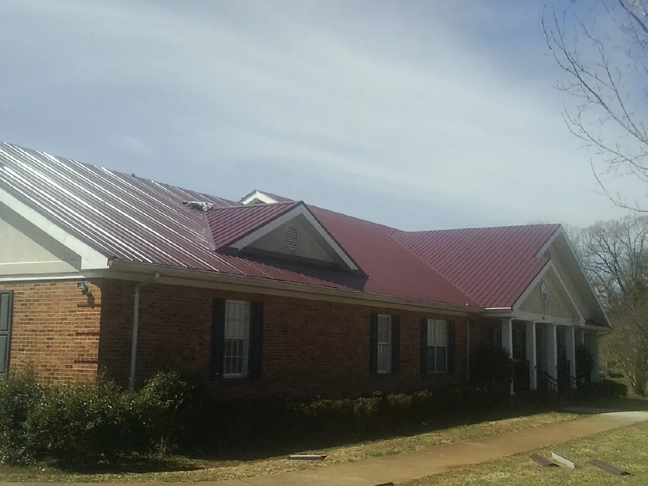 Red metal roof with gabled entries on a long brick building, from a Hail Damage Roof Repair job in Teton