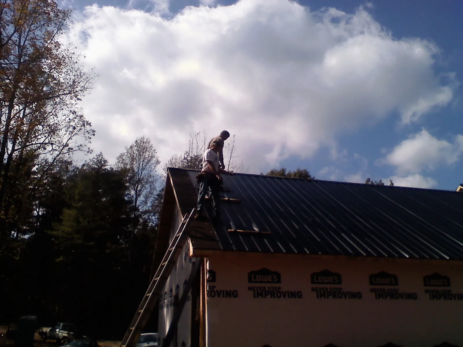 Roofer fastening dark metal panels high against a cloudy sky, from a Roof Inspection job in Teton