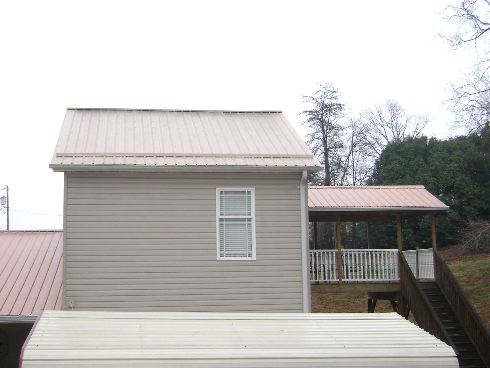 Tan metal roofs on a two story addition and attached porch, from a Roof Replacement job in Teton